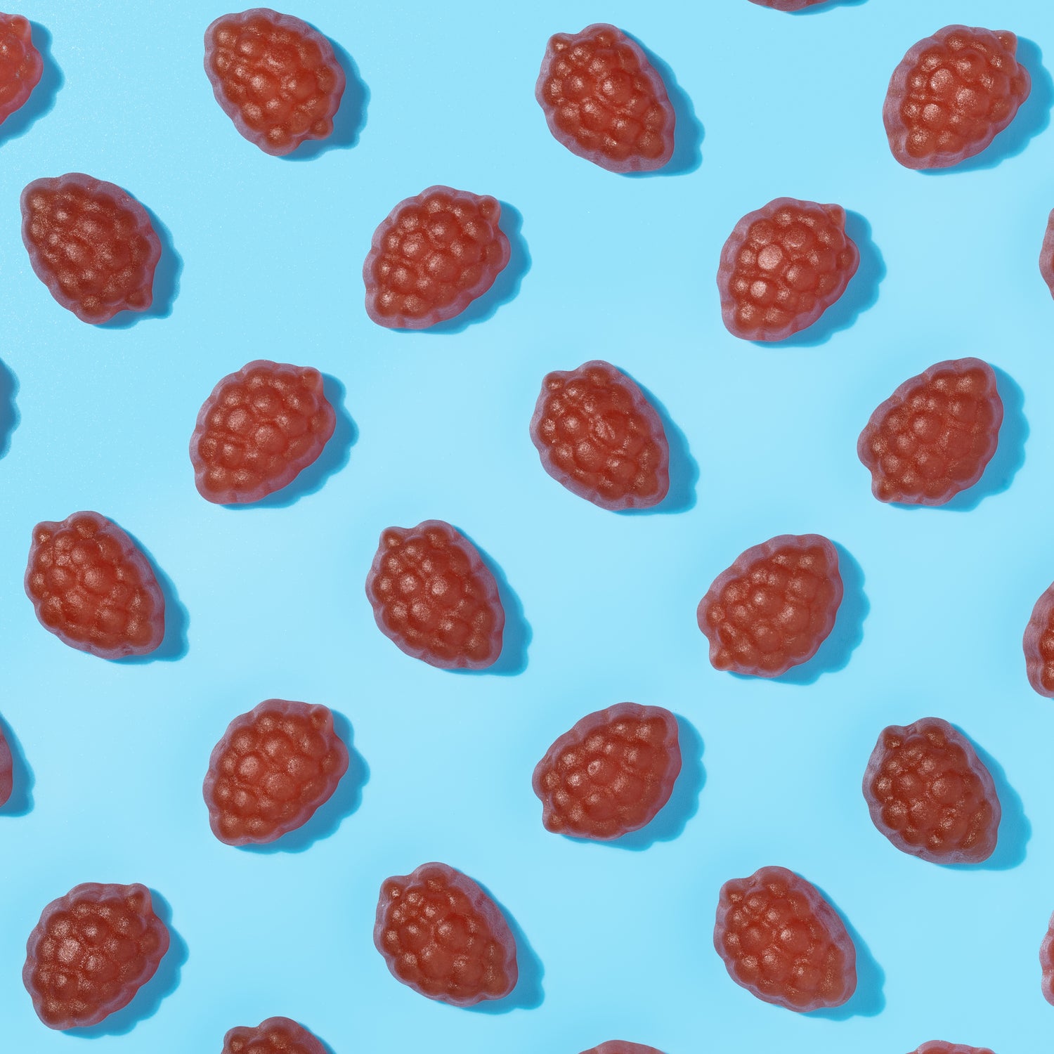 Red gummy candies shaped like raspberries on a blue background.