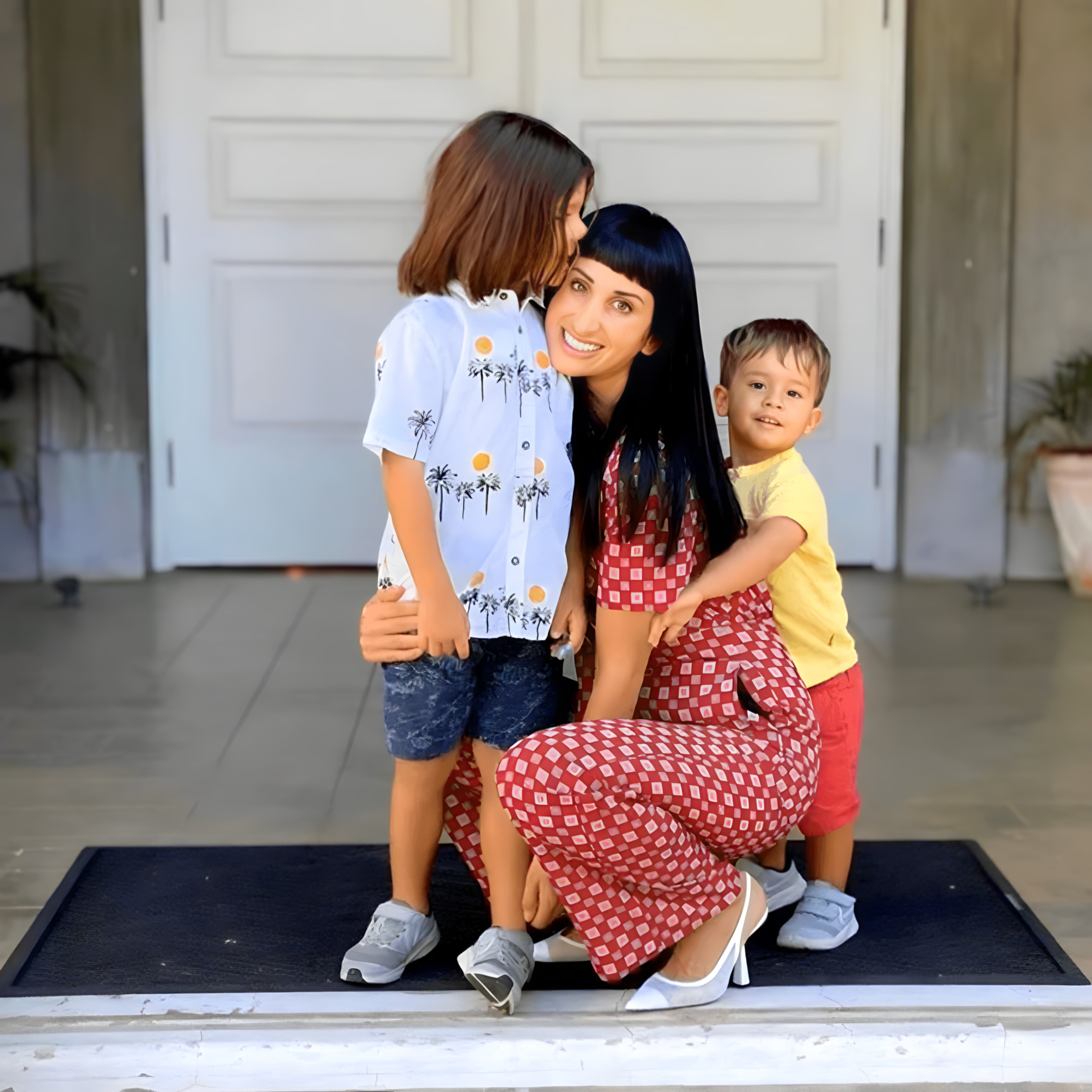 Smiling mother kneeling with her two young children outdoors, capturing a warm family moment together.