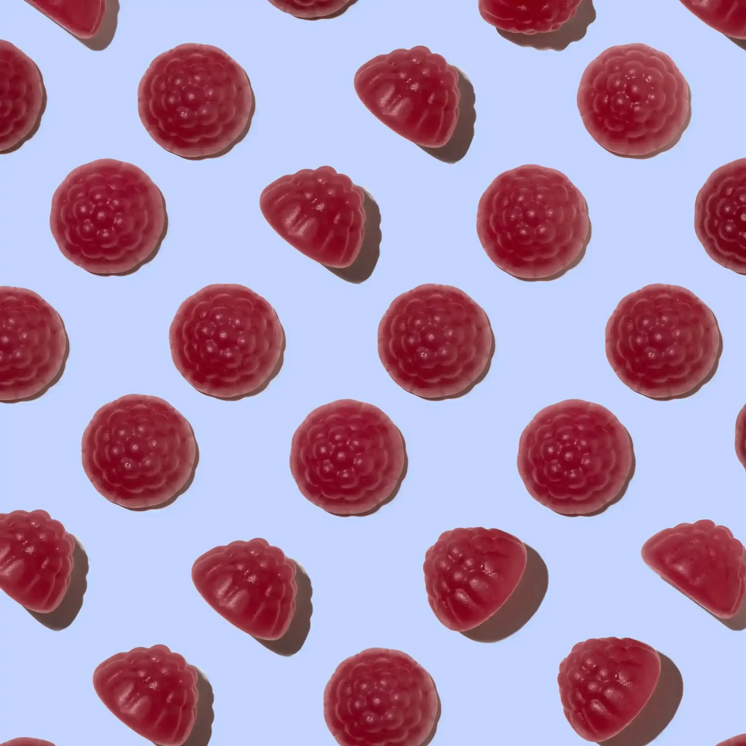Pattern of red gummy raspberries shaped gummies on a light blue background